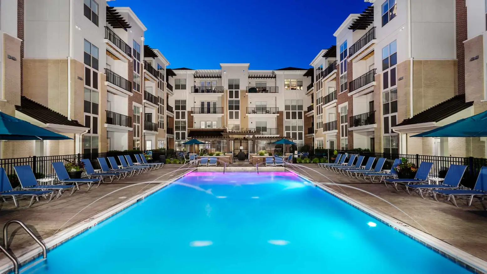 Luxury swimming pool lit up at night with water features and underwater lights.