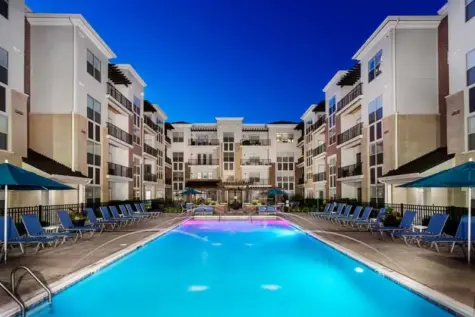 Luxury swimming pool lit up at night with water features and underwater lights.