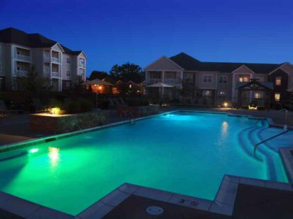 Beautiful pool area next to clubhouse with lounge chairs lit at night.