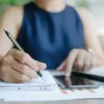 A businesswoman using a smartphone and taking notes.