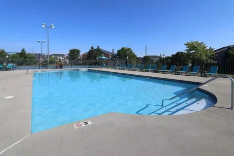 A large pool surrounded by patio chairs with apartment buildings in the background.