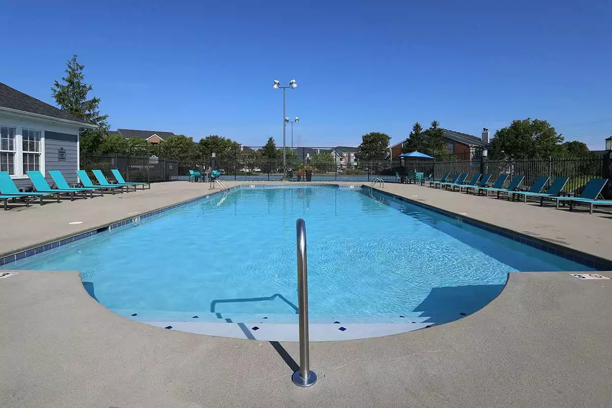 A large pool surrounded by patio chairs with large apartment buildings in the background.