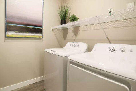 Small laundry room featuring a washer and dryer with overhead shelving.