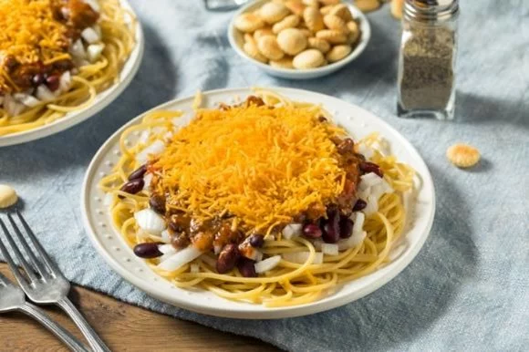A plate of skyline chili next to silverware and crackers.