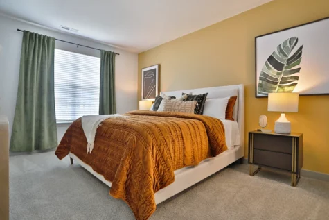 Graphite Oakley Apartments bedroom with upscale decor with mustard yellow bedspread, leaf wall decor and spacious floor plan