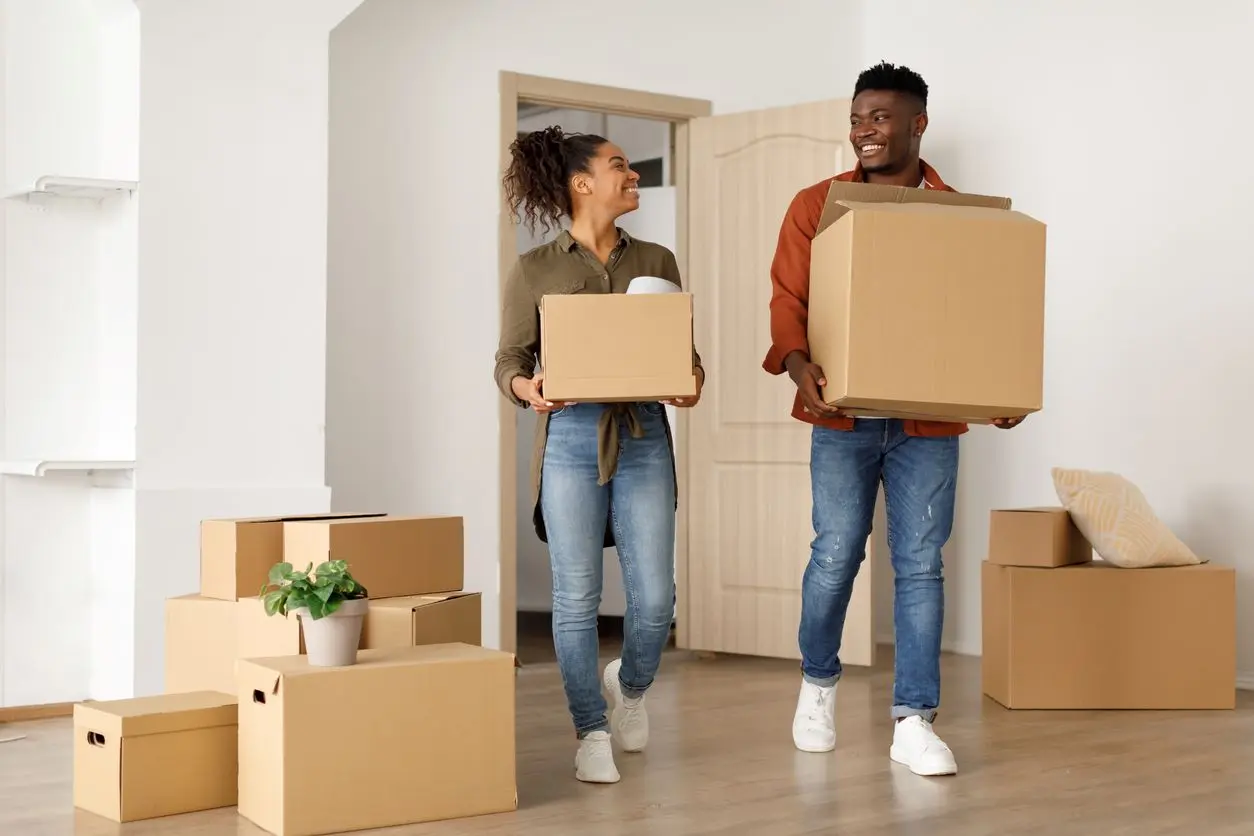 Two smiling young adults carrying boxes on moving day.