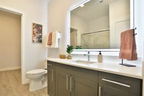 Master bathroom. Sink, lit mirror, toilet, wooden floors. Clocktower Apartments in West Chester, OH