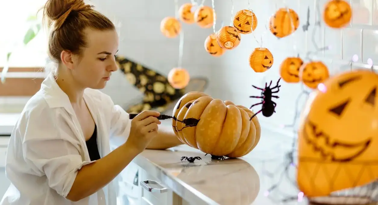 A young woman decorates for Halloween by drawing a face on a pumpkin.