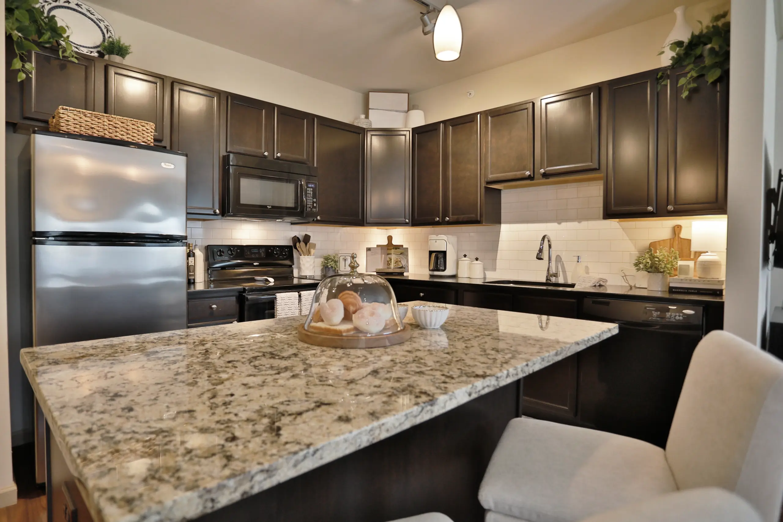 Palmera Apartments luxury kitchen. Seated area with granite countertops. Dark wood colored cabinets and stainless steel appliances.