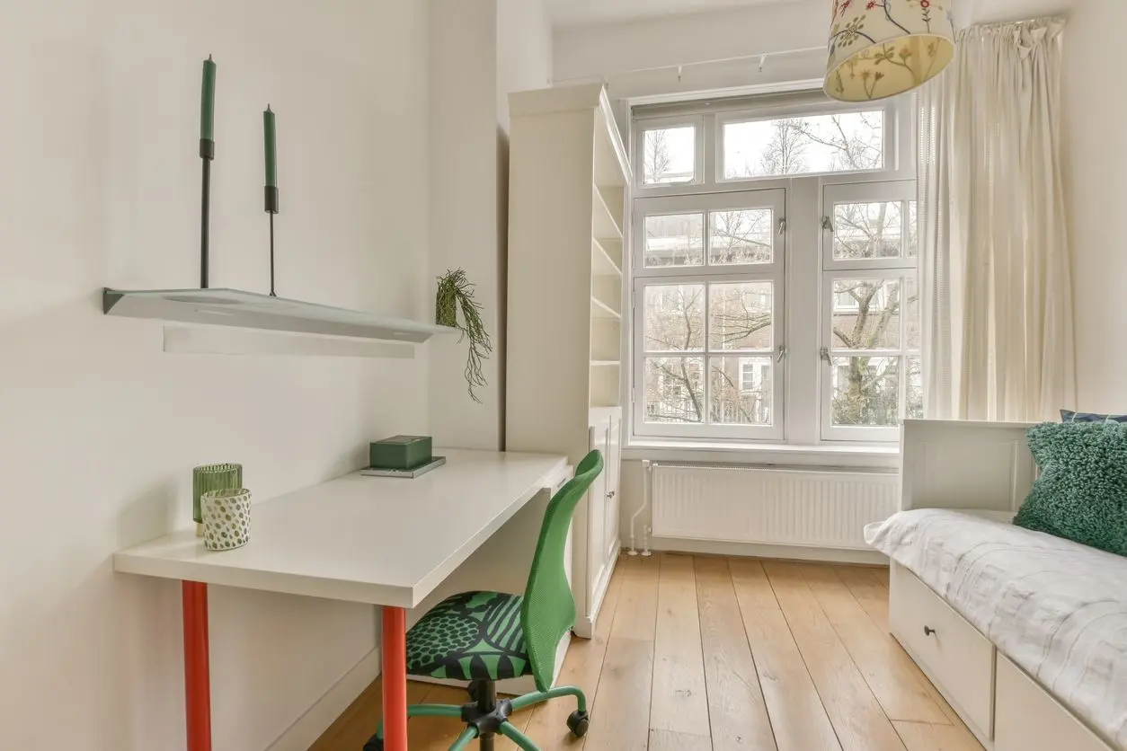 A minimalist spare bedroom with a desk, daybed, bookshelf, and large windows.