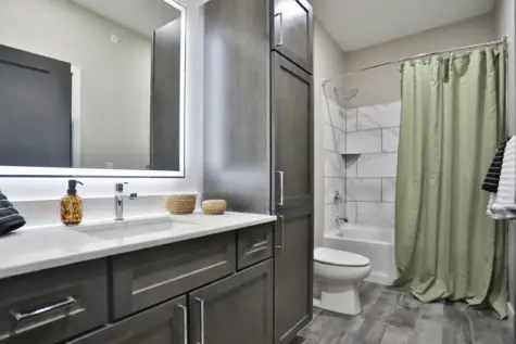 Master bathroom with quartz countertops, large lit mirror and tiled shower at Altair Apartments in Florence, KY
