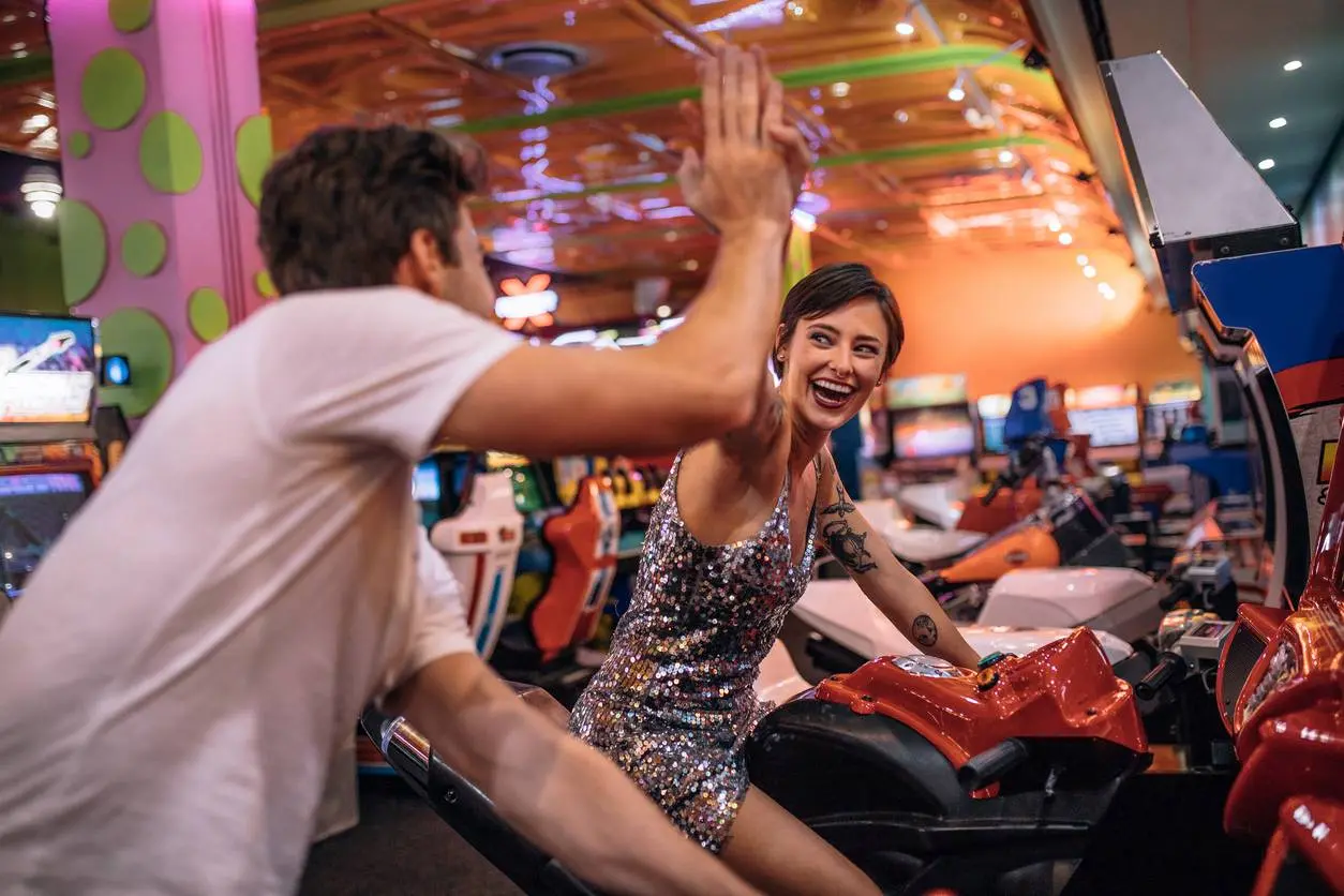 A smiling, high-fiving couple plays a racing arcade game.