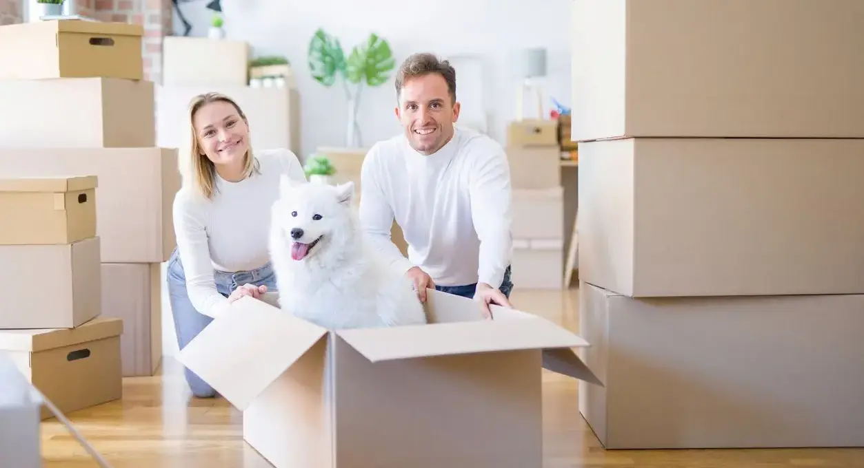 A smiling couple signs a clipboard from a duo of movers.