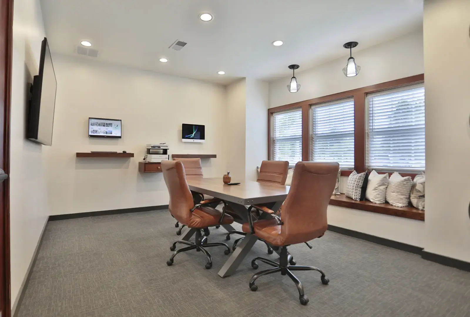 Business center at Wellington Place Apartments featuring Mac and PC workstations, a conference table, wireless printing, and charging stations in a modern, professional setting.