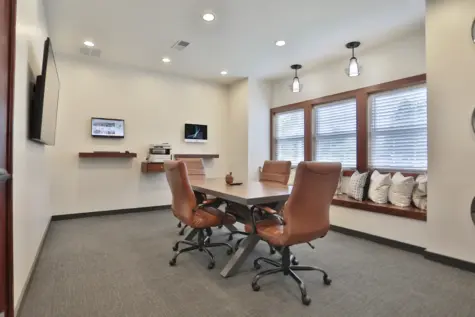 Business center at Wellington Place Apartments featuring Mac and PC workstations, a conference table, wireless printing, and charging stations in a modern, professional setting.