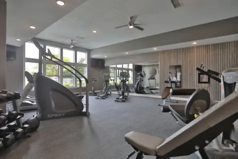 Fitness center at Wellington Place Apartments featuring cardio machines like treadmills and a StairMaster, a Mirror personal trainer, multifunctional weight machines, and free weights in a spacious, modern setting.
