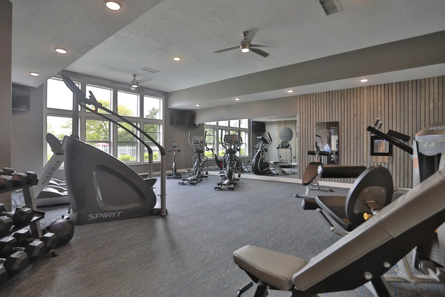 Fitness center at Wellington Place Apartments featuring cardio machines like treadmills and a StairMaster, a Mirror personal trainer, multifunctional weight machines, and free weights in a spacious, modern setting.