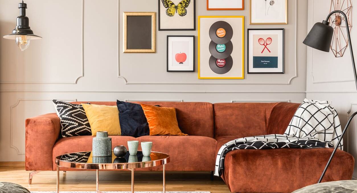 Eclectic style living room with funky art on the walls, an orange couch, and warm toned pillows.