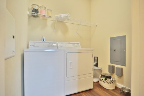 Utility room at Kendal on Taylorsville including a full-size washer and dryer with convenient shelving and storage.