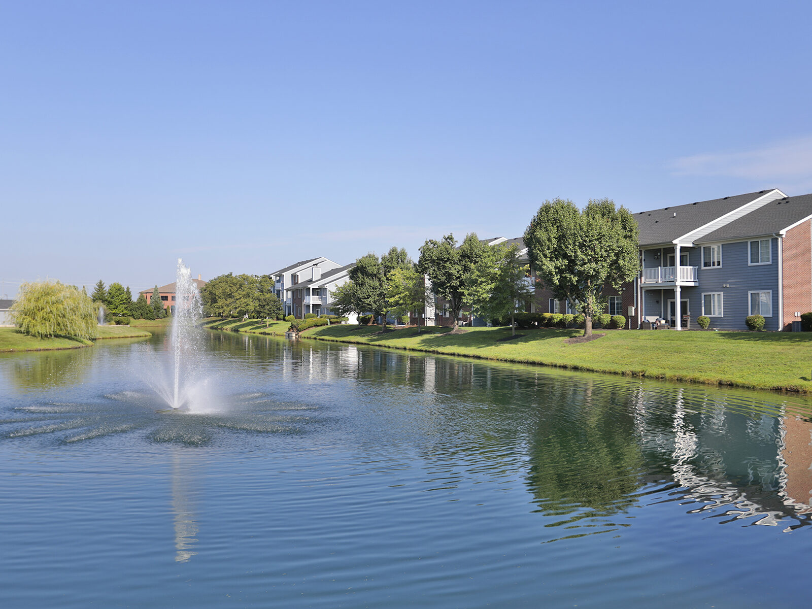 Scenic pond view with reflection of two- and three-story apartment buildings at The Landings at Beckett Ridge.