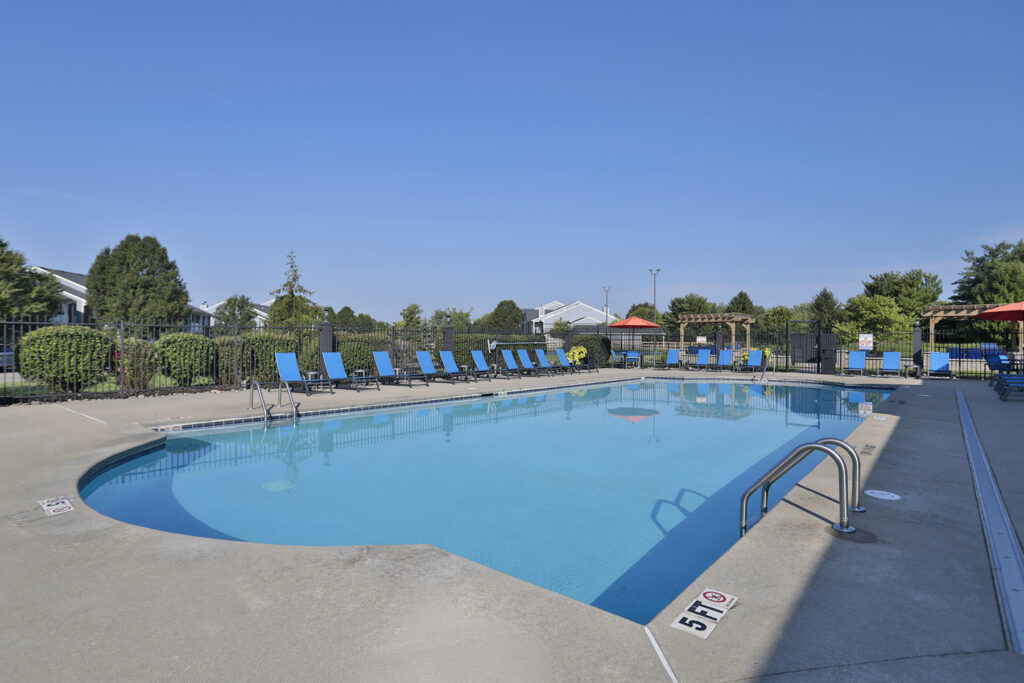 Community swimming pool with expansive sundeck and comfortable outdoor seating, perfect for relaxing on sunny days.