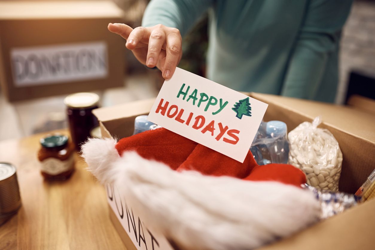 A woman places a holiday card into a donation box filled with items, including a Santa hat.