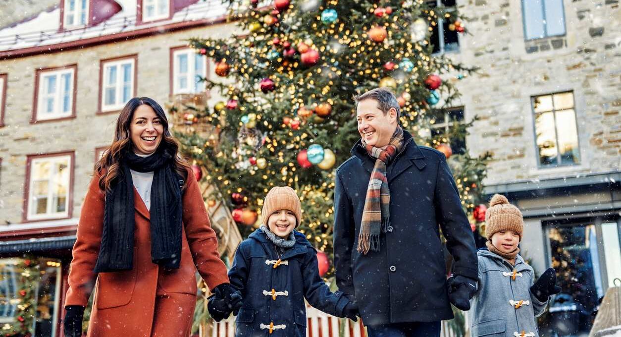 A happy family of four smiles together as they walk away from a decorated Christmas Tree.