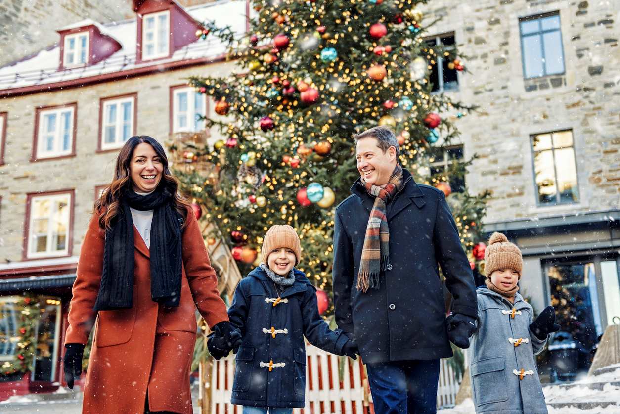 A happy family of four smiles together as they walk away from a decorated Christmas Tree.