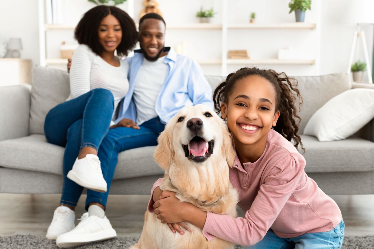 Two parents smile as their daughter hugs their family dog in their luxury pet-friendly apartment.