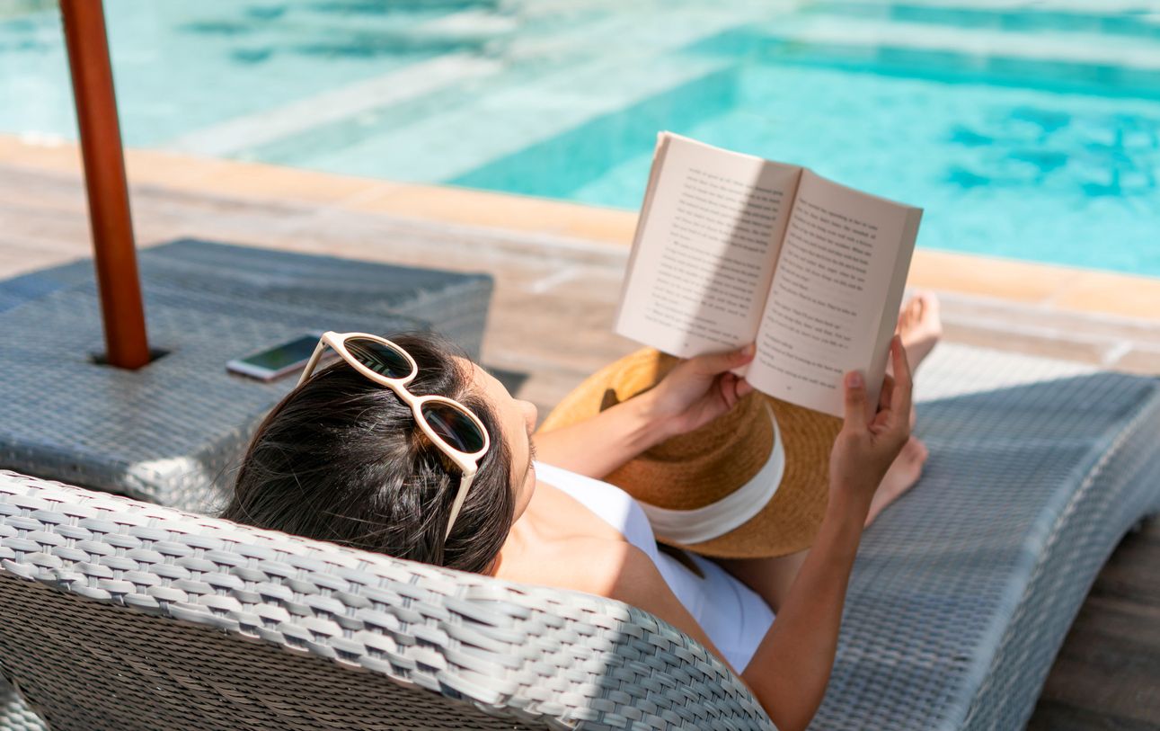 A woman reads her book by the pool, one of the many luxury apartment amenities you can enjoy.