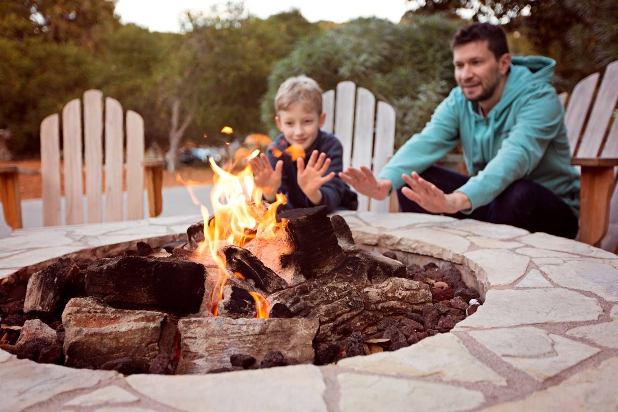 A father and son sit together and smile while enjoying the warmth of their luxury apartment firepit