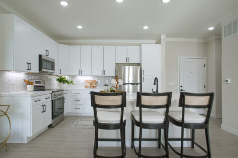 Modern kitchen at Relay 129 with white quartz island, stainless steel appliances, tile backsplash, large capacity sink, matte black plumbing fixtures, grey and white cabinetry, and island bar seating.
