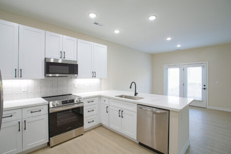 Modern kitchen in 3 bedroom townhome at Relay 129 featuring white quartz island with bar seating, stainless steel appliances, tile backsplash, large capacity sink, matte black fixtures, and grey cabinetry.