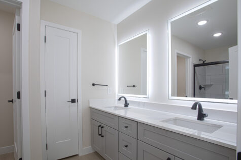 Modern primary bathroom with sliding glass shower door, white quartz double vanity, LED mirror, and matte black hardware at Relay 129.