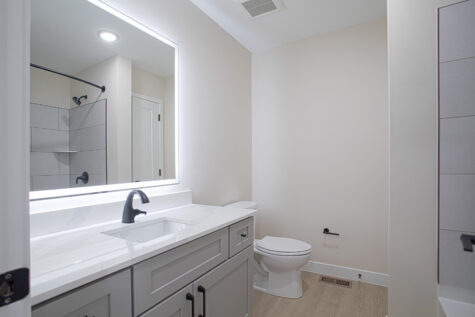 Primary bathroom in 3 bedroom townhome at Relay 129 featuring soaking tub, white quartz vanity, LED backlit mirror, matte black fixtures, and grey cabinetry.