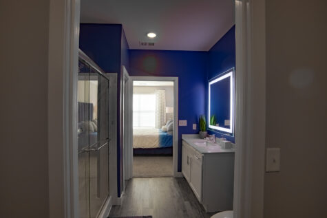 Contemporary bathroom hallway at Allure in Centerville, Ohio by Hills Properties featuring illuminated vanity mirror, walk-in glass shower, wood-look flooring, and modern designer finishes.