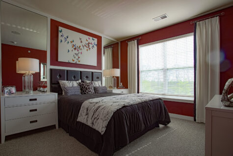Contemporary bedroom at Allure in Centerville, Ohio by Hills Properties featuring plush carpeting, oversized windows, mirrored accents, designer lighting, and bold accent walls.