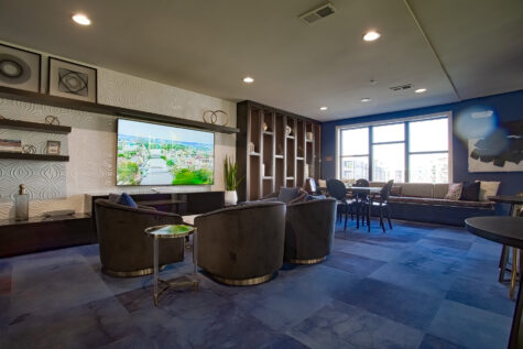 Resident social lounge at Allure Apartments with large TV, contemporary furnishings, dining tables, and floor-to-ceiling windows.