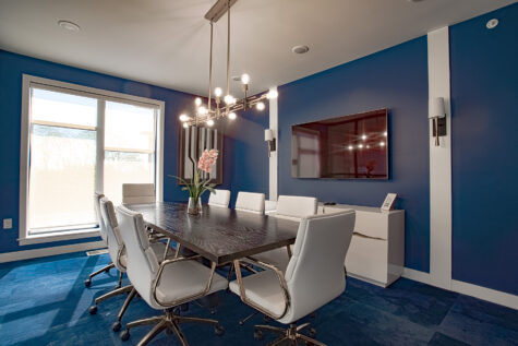 Private conference room at Allure Apartments with dark wood table, white leather chairs, mounted TV, and modern blue accent walls.