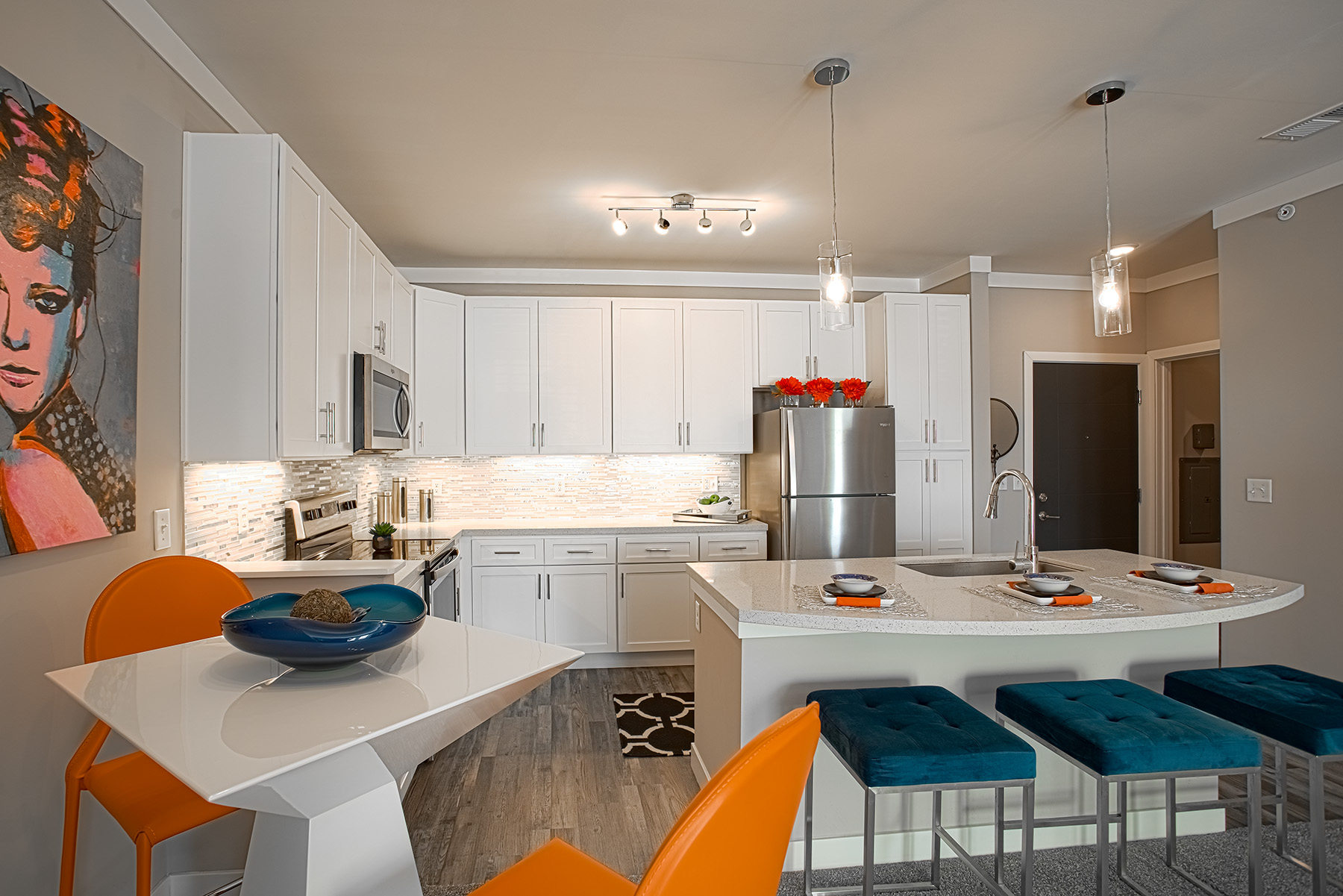 Open-concept kitchen and dining area at Allure in Centerville, Ohio by Hills Properties featuring white cabinetry, stainless steel appliances, oversized breakfast bar seating, modern lighting, and contemporary furnishings.