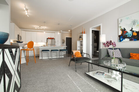 Spacious apartment interior at Allure Apartments by HILLS Properties showcasing a stylish living room, glass coffee table, contemporary artwork, open kitchen with quartz countertops, and modern neutral finishes.