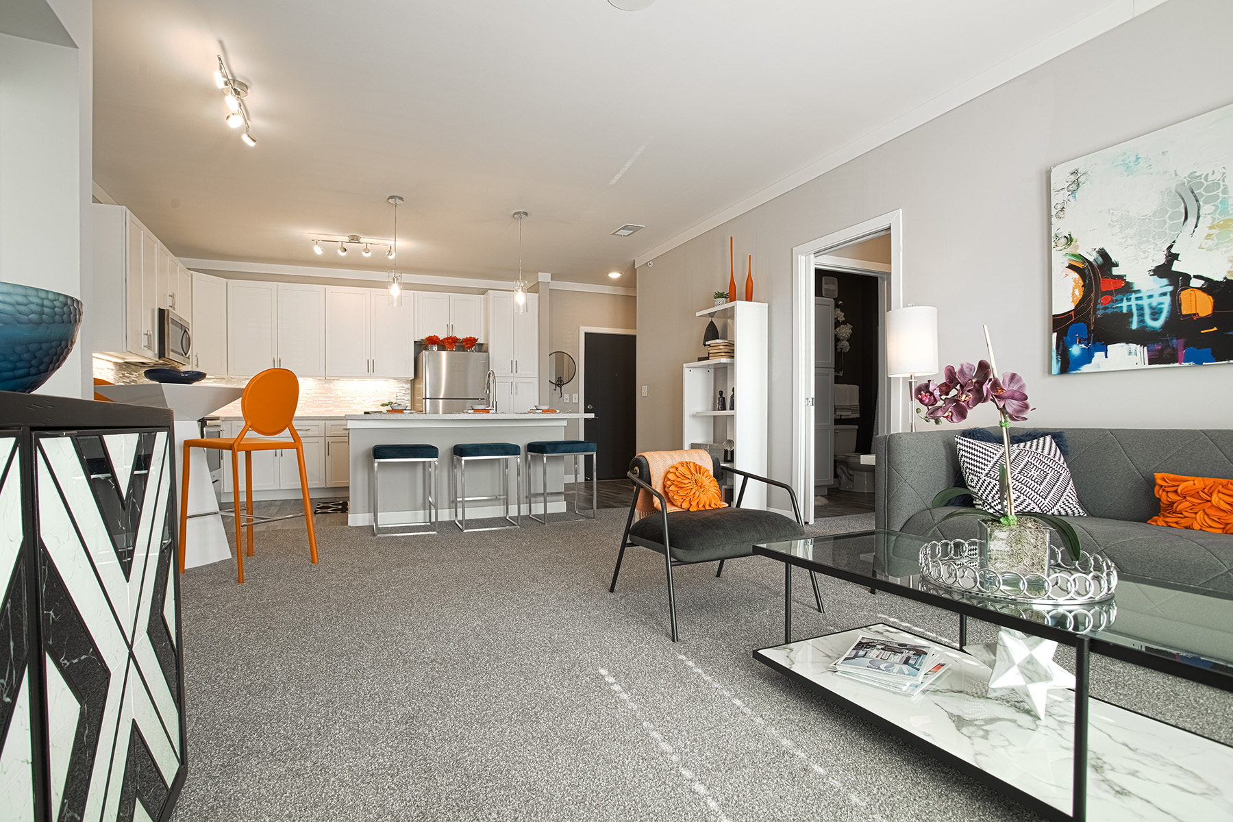 Spacious apartment interior at Allure Apartments by HILLS Properties showcasing a stylish living room, glass coffee table, contemporary artwork, open kitchen with quartz countertops, and modern neutral finishes.