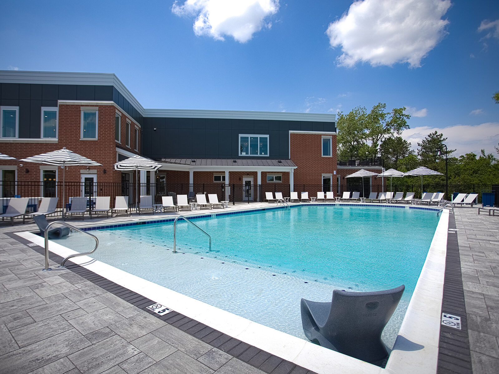 Resort-style swimming pool with in-water lounge seating, shaded umbrellas, and modern clubhouse exterior at Relay 129 by HILLS Properties in Liberty Township, Ohio.