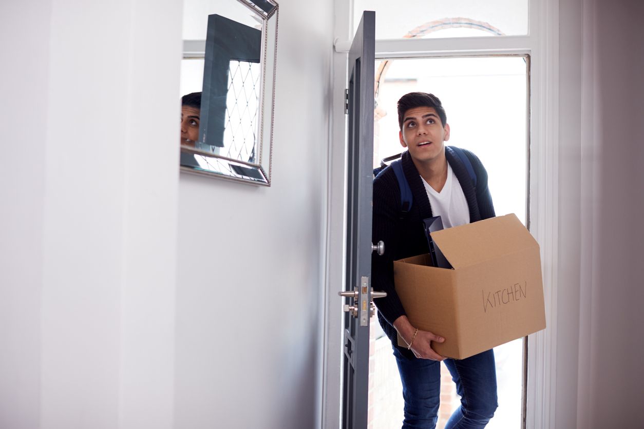 A man carrying a box moves into his ground-level apartment, entering from the street.