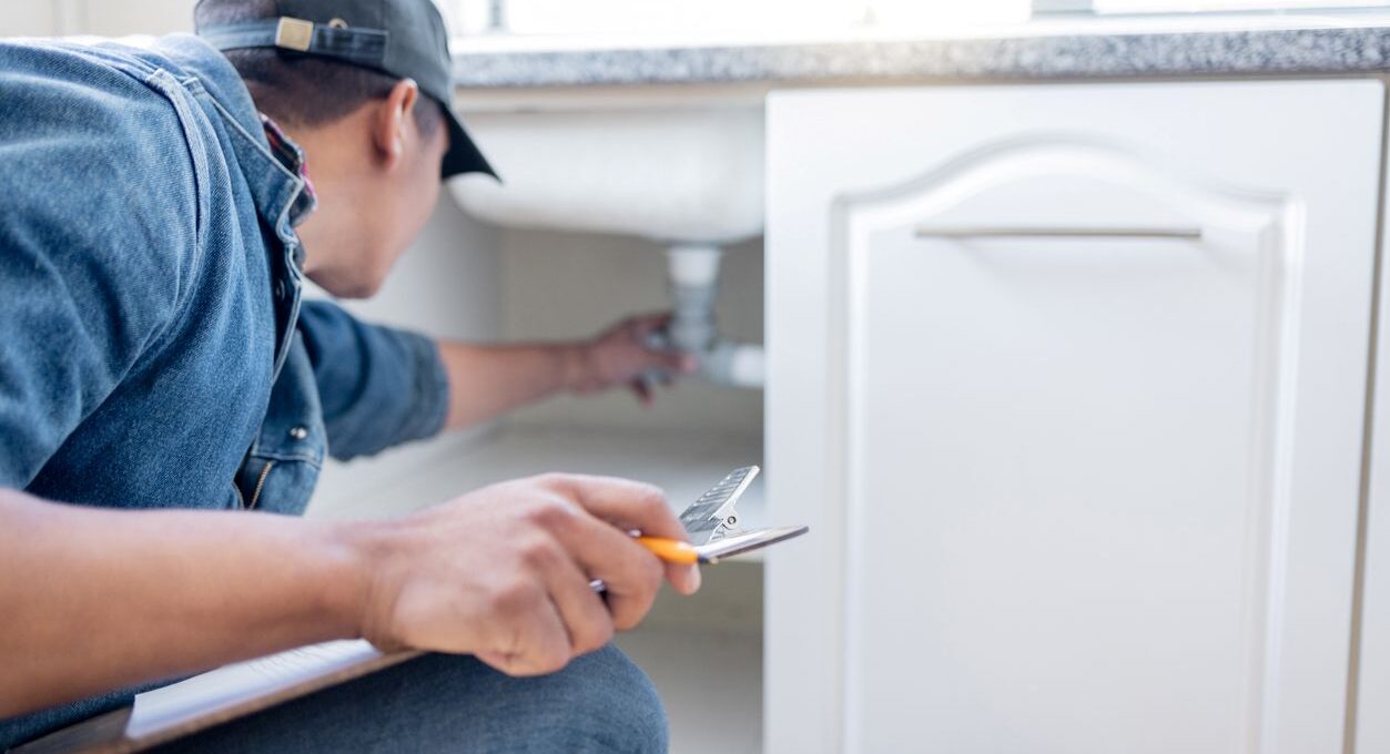 An apartment maintenance technician inspects the plumbing under the sink in a resident’s home.