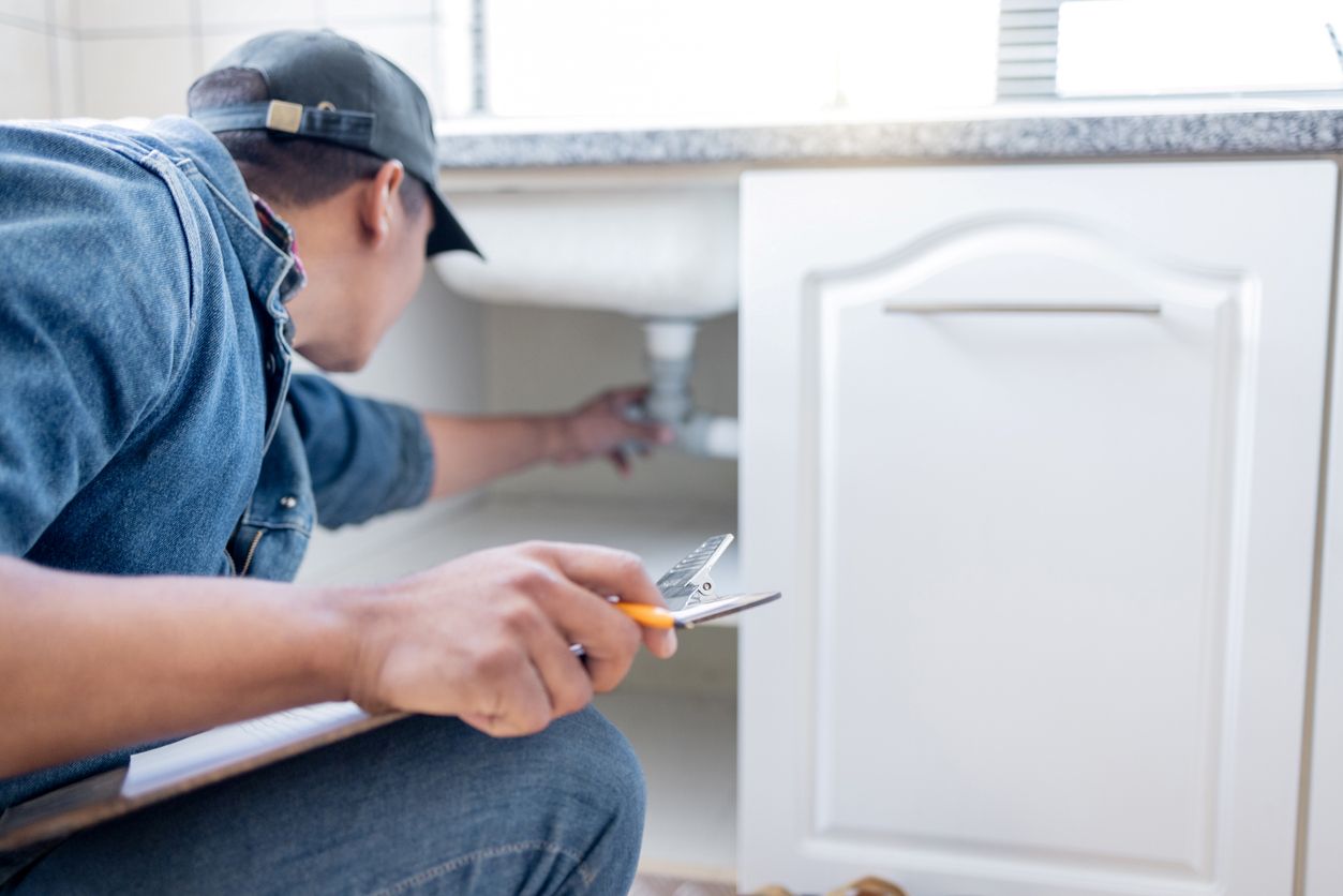 An apartment maintenance technician inspects the plumbing under the sink in a resident’s home.