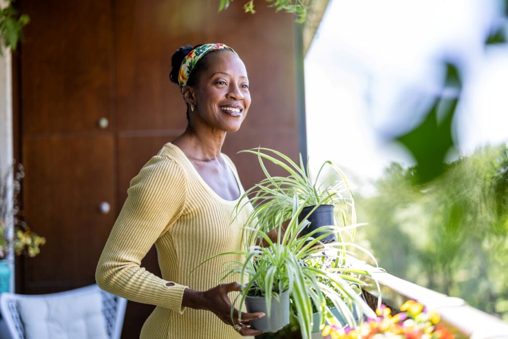 A woman smiles as she waters her plants on her second-floor apartment balcony.