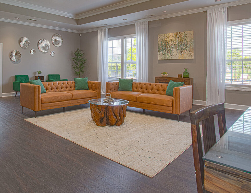 Spacious resident clubhouse lounge at Emerald Lakes in Greenwood, Indiana, showcasing modern leather seating, large windows with natural light, high ceilings with recessed lighting, and contemporary décor by HILLS Properties.