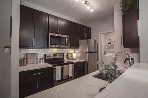 Contemporary kitchen at Sterling Lakes by HILLS Properties featuring dark espresso cabinetry, stainless steel appliances, quartz countertops, subway tile backsplash, and a convenient view into the in-home laundry area.