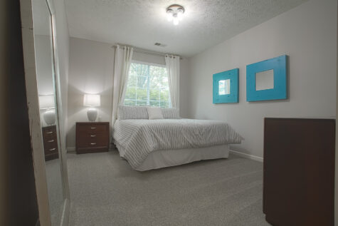 Spacious bedroom at Sterling Lakes by HILLS Properties in Mason, Ohio with plush carpeting, neutral finishes, dark wood furnishings, and large windows providing natural light.
